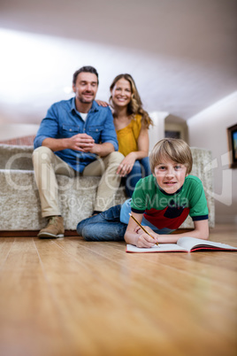 Boy doing homework while parents sitting on sofa in background