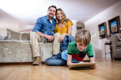 Boy using a digital tablet while parents sitting on sofa in back