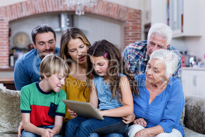 Multi-generation family sitting on sofa and using digital tablet