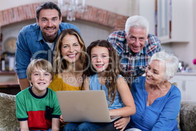 Multi-generation family sitting on sofa and using laptop