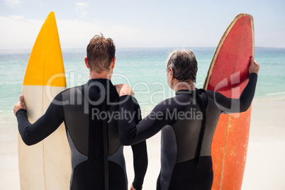 Father and son with surfboard standing on beach