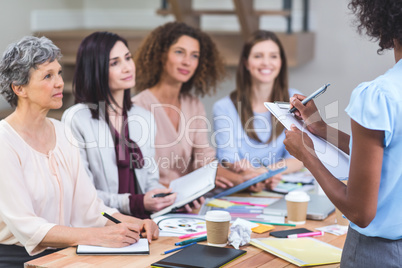 Woman noting on clipboard while colleagues listening presentatio