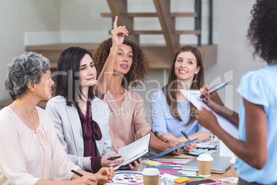 Woman noting on clipboard while colleagues listening presentatio