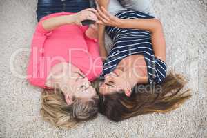 Two beautiful women lying on rug looking at the mobile phone
