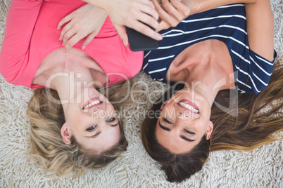 Two beautiful women lying on rug and looking at the mobile phone