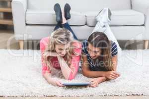 Two beautiful women lying on rug and using digital tablet