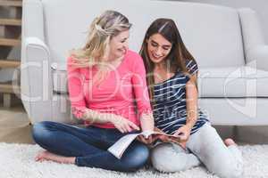 Two beautiful women looking at a magazine in living room