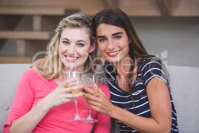 Two beautiful women holding glass of wine and talking in the liv