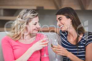 Two beautiful women holding glass of wine and talking in the liv