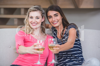 Two beautiful women showing their glass of wine in the living ro