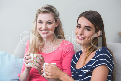 Two beautiful women sitting side by side with a mug of coffee