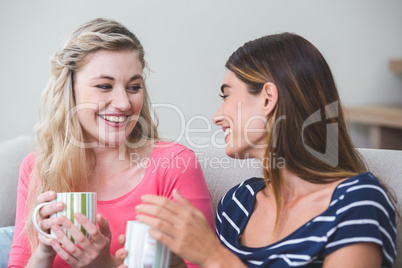 Two beautiful women holding a cup of coffee and talking in the l