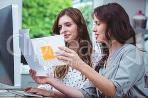 Two woman looking at document and using computer