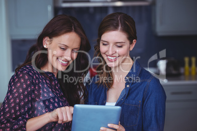 Two beautiful women using digital tablet in kitchen