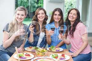 Friends holding glass of red wine while having meal