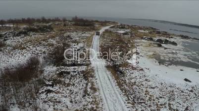 Flying over minivan driving on winter shore