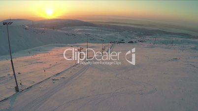 Ski-run and snowy hills at sunset, aerial view