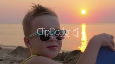 Cute boy in sunglasses on the beach at sunset