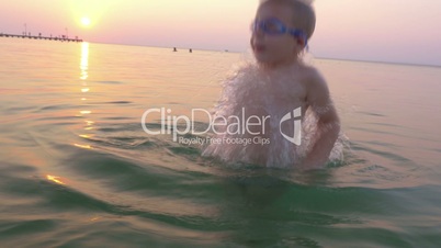 Little child in goggles having fun in sea during sundown