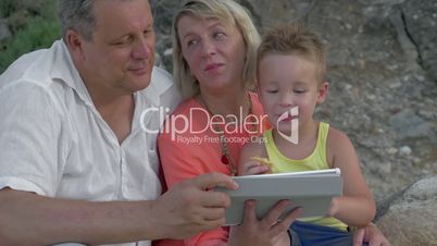 Mother,father and son watching video on pad while sitting on beach