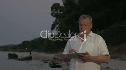 Senior man using tablet PC on beach in late evening