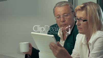 Woman using tablet, man drinking coffee