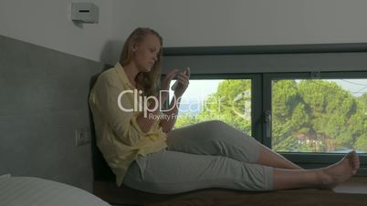 Woman sitting on window-sill and using phone