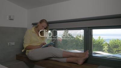 Smiling Woman with Tablet on Window Sill