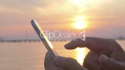Man typing on smartphone by sea at sunset