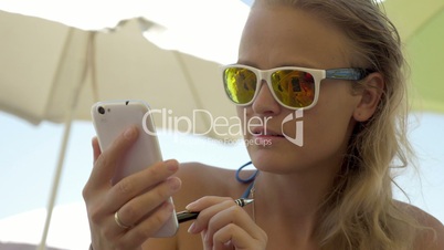Woman in sunglasses using cell on beach