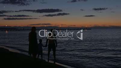 Parents and child walking by the sea in dusk
