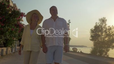 Senior couple walking on sea-front at sunset