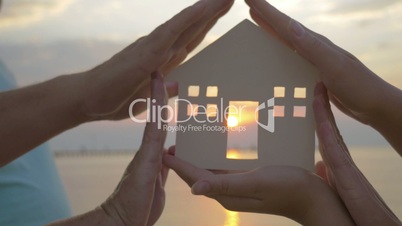Hands Holding House Silhouette against Sun