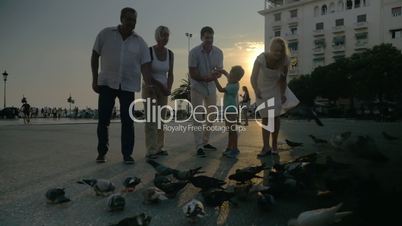 Family and flock of pigeons in the street at sunset