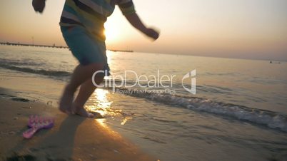 Child running barefoot along the sea at sunset
