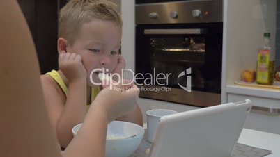 Mother feeding child while he watching tablet PC