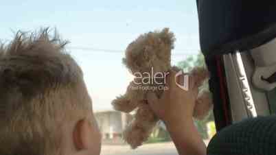 Little child with teddy bear looking out car window