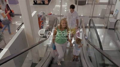 Young family with child riding escalator in shopping center