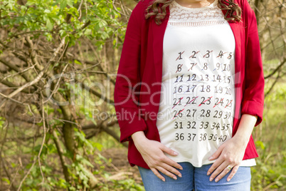 Pregnant woman in red jacket with calendar on her T-shirt outdoo