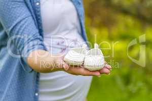 Close up of pregnant woman hand with baby shoes