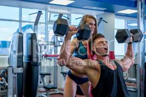 Girl helps muscular guy to exercise with dumbbells