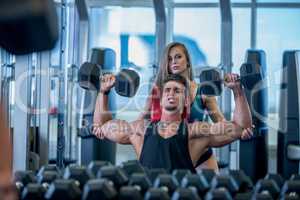 Girl insures guy during exercising with dumbbells