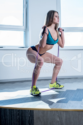 In gym. Sporty woman doing squats using expander