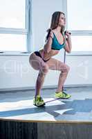 In gym. Sporty woman doing squats using expander