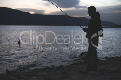 Man fishing on mountain lake. Sunrise low light.