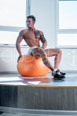 Tattooed bodybuilder sitting on fitness ball