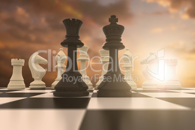 Composite image of black king and queen standing in front of white pieces