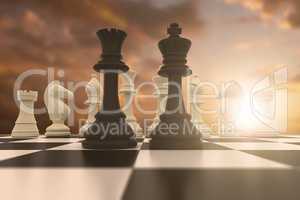 Composite image of black king and queen standing in front of white pieces