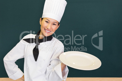 Composite image of smiling female cook holding empty plate in kitchen