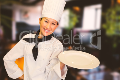 Composite image of smiling female cook holding empty plate in kitchen